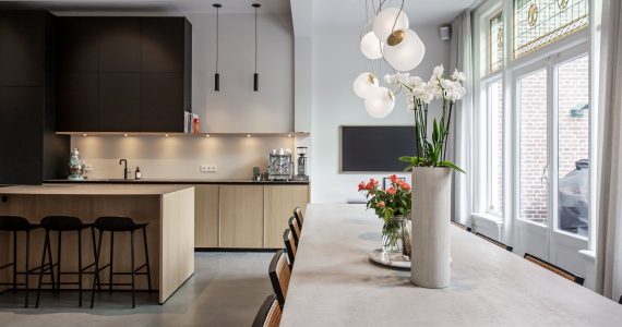 woonbeton van Willem Designvloeren in een moderne keuken in een herenhuis van de vorige eeuw gecombineerd met karakteristieke elementen zoals glas-in-lood ramen en sierlijsten aan het plafond.