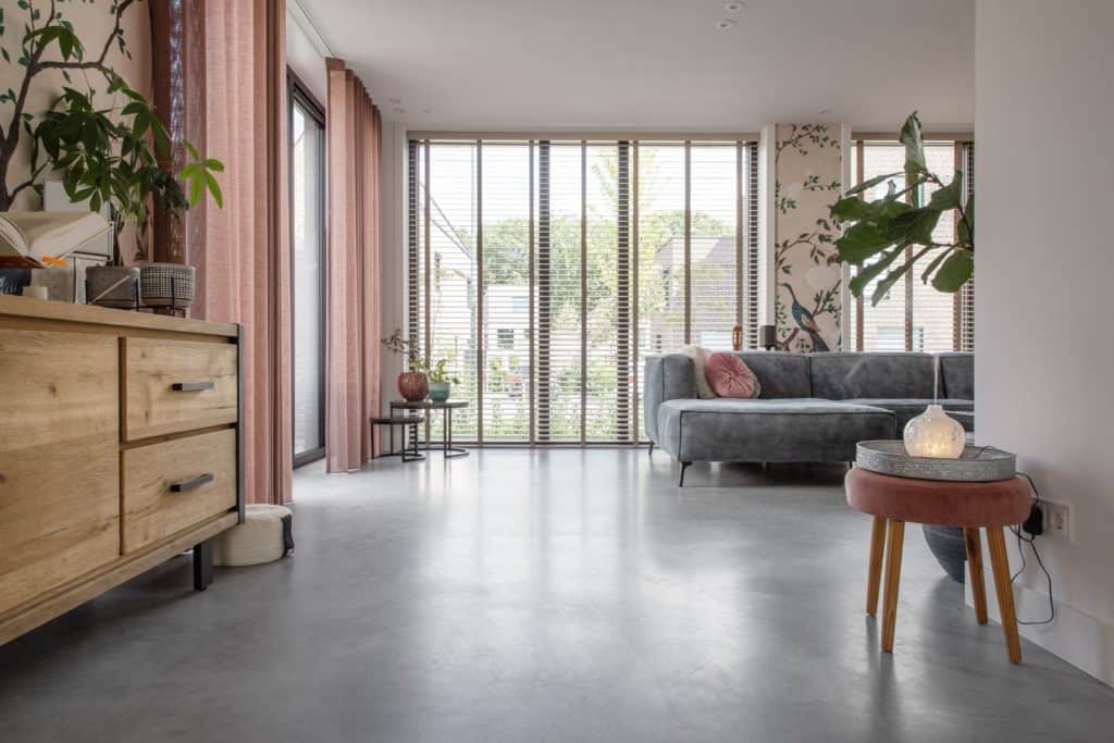 Woonkamer in Ede gecombineerd met een grijze bank, roze gordijnen en een gevlinderde betonvloer