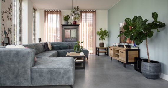 Woonkamer in Ede met een grijze bank, roze gordijnen, een houten tv-meubel en een gevlinderde betonvloer