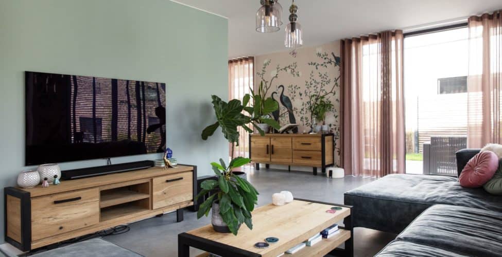 Woning in Ede met een gevlinderde betonvloer in de woonkamer, hierin staat een grijze bank, een houten bijzettafel en een houten tv-meubel