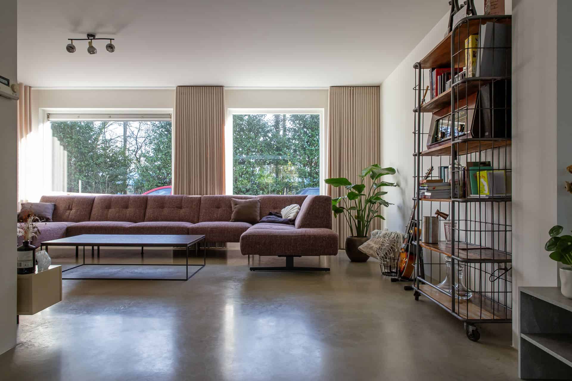 Woonkamer met een gevlinderde betonvloer in Sprang-Capelle. Ook staat er een plant op de vloer en een kast met wat boeken en accessoires.