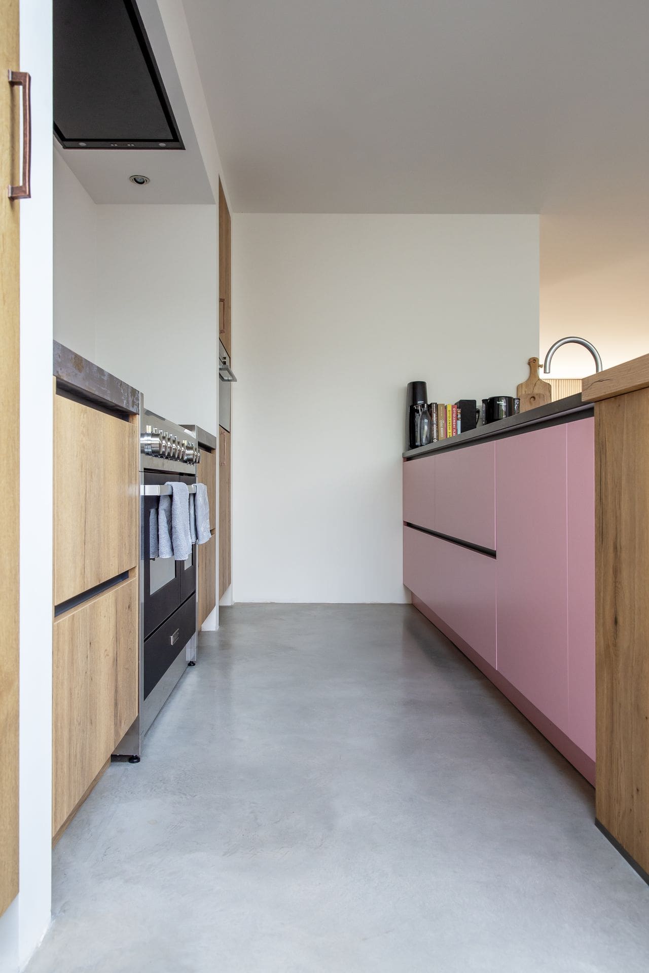 Houten keuken met wat roze keukenkastjes in Sprang-Capelle. Dit staat op een gevlinderde betonvloer.