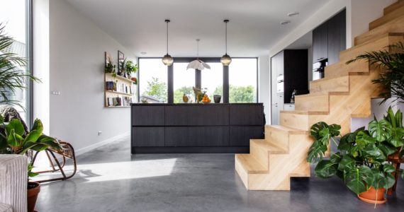 Zwarte keuken in Zijdewind met daarvoor een houten trap. Dit is gecombineerd met een gevlinderde betonvloer