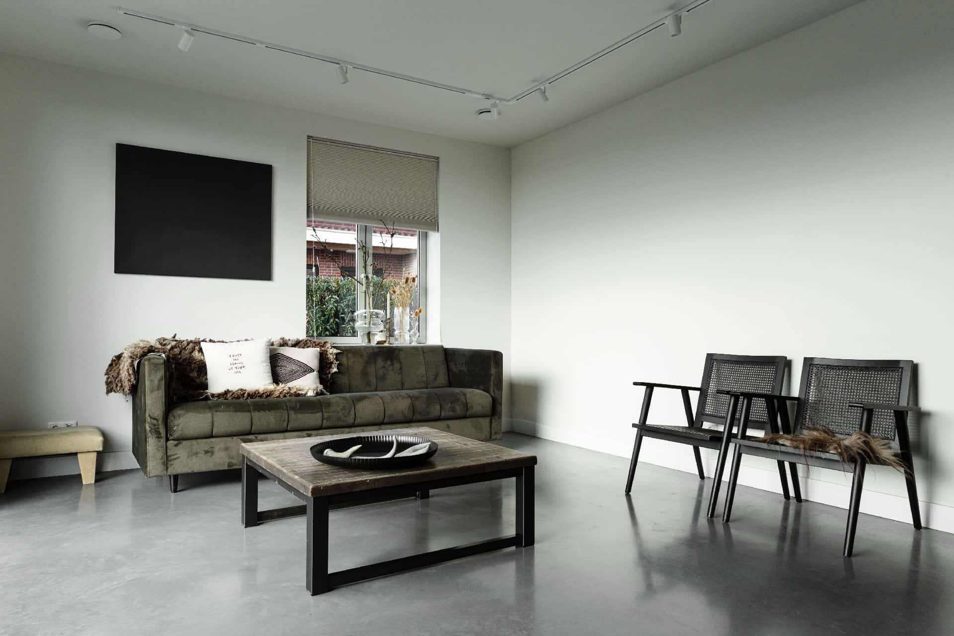Vrijstaande woning in Brandwijk met een gevlinderde betonvloer in de woonkamer. Hierop staat een groene velvet bank en twee zwarte stoelen.