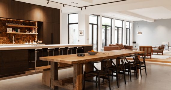 Gevlinderde betonvloer in Den Haag. Deze ligt in de keuken. De keuken is bruin en er staat een kookeiland met 5 barkrukken. De tafel is van hout met daaraan een houten bankje en vier stoelen.