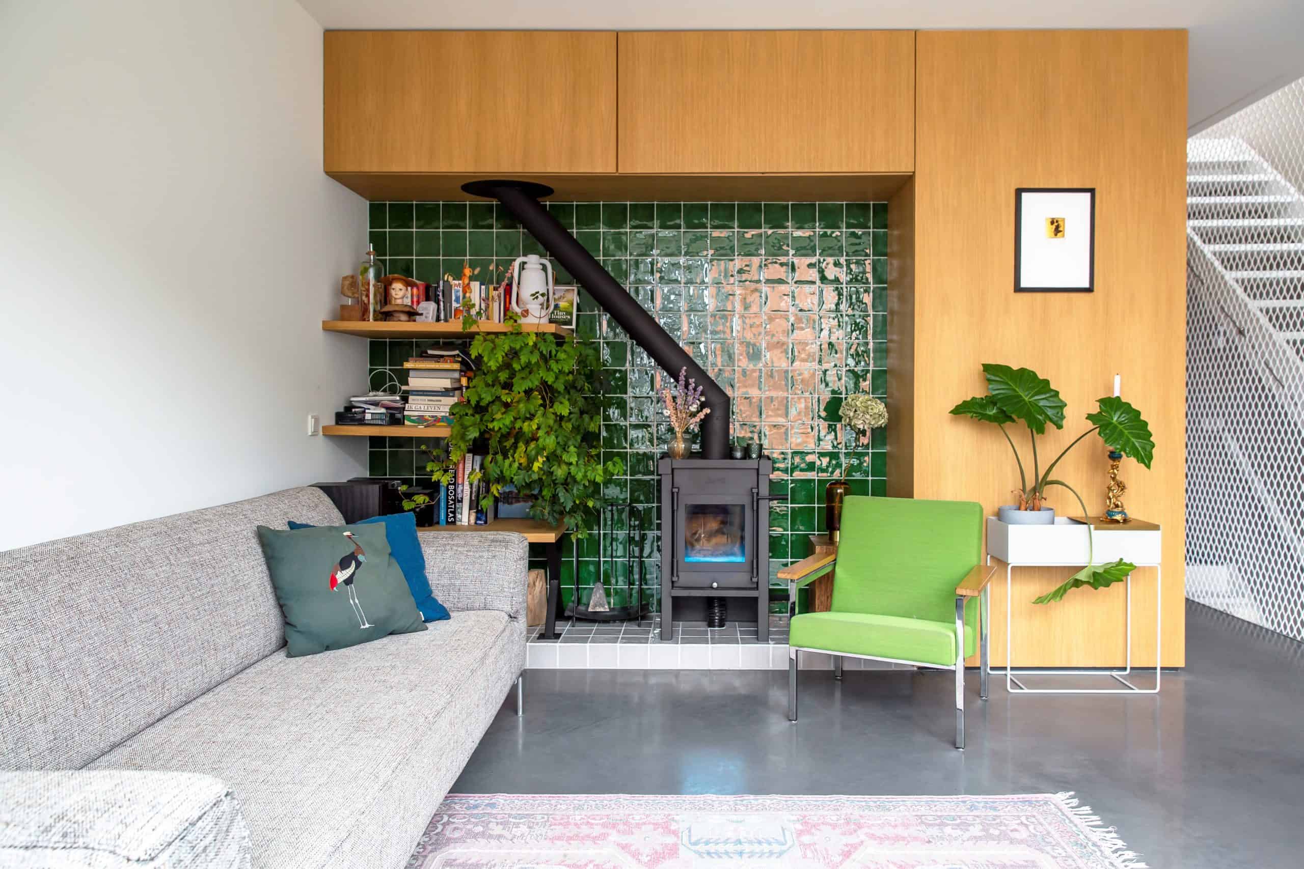 Woonkamer in Amsterdam met een grijze bank. groene stoel en een groene muur. Op de grond ligt een kleed over een gevlinderde woonbetonvloer.