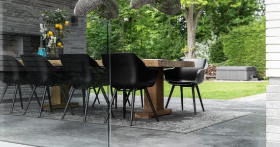 Gevlinderd betonnen terras in Heemstede met hierop een grijs vloerkleed, een houten tafel en 8 zwarte stoelen.