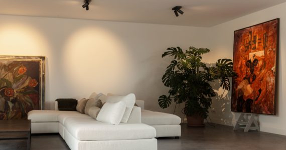 Gevlinderde betonvloer in de woonkamer, gecombineerd met een lichte bank en kunst.