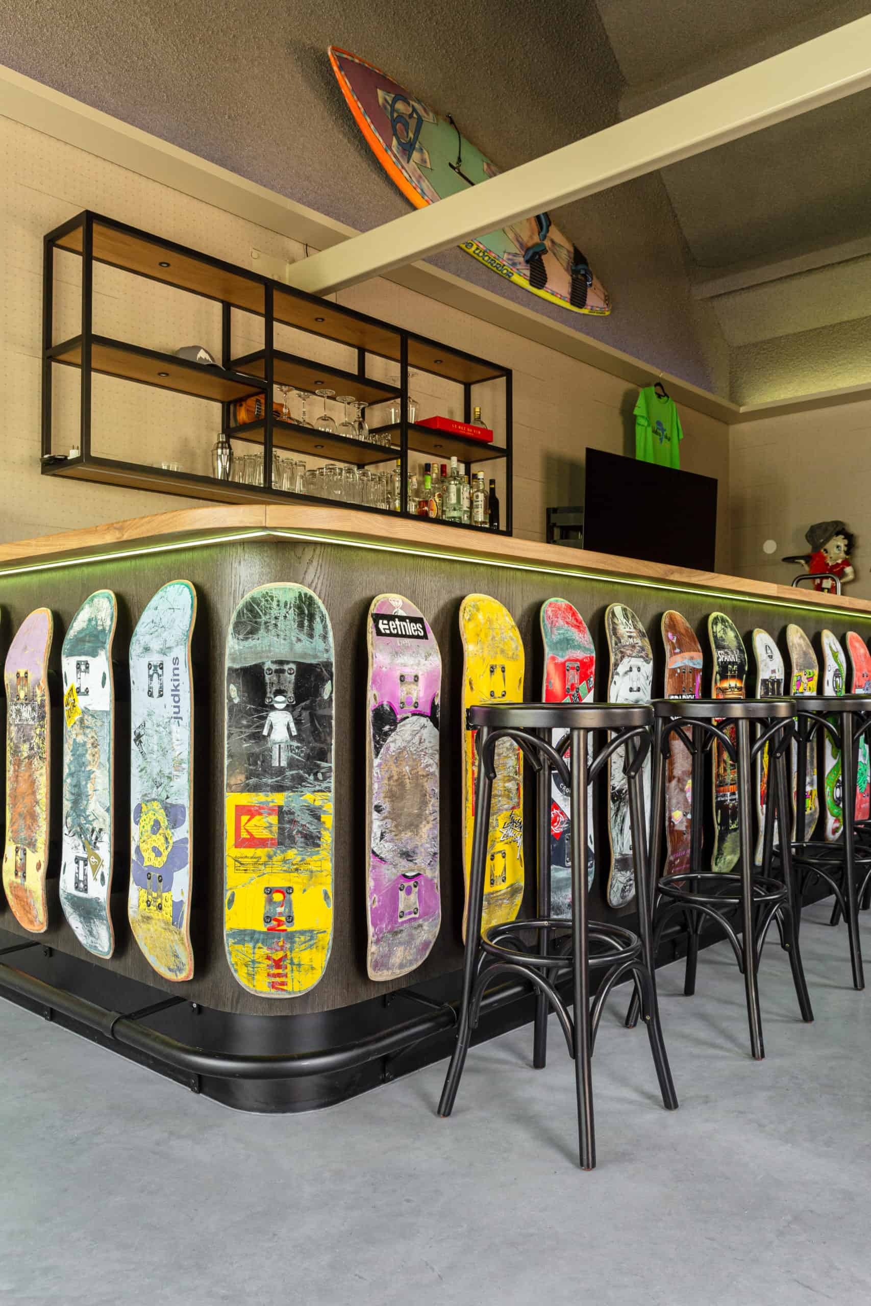 De bar in Oss. Deze is omringd met skateboards en er staan barkrukken omheen. De vloer is een gevlinderde betonvloer