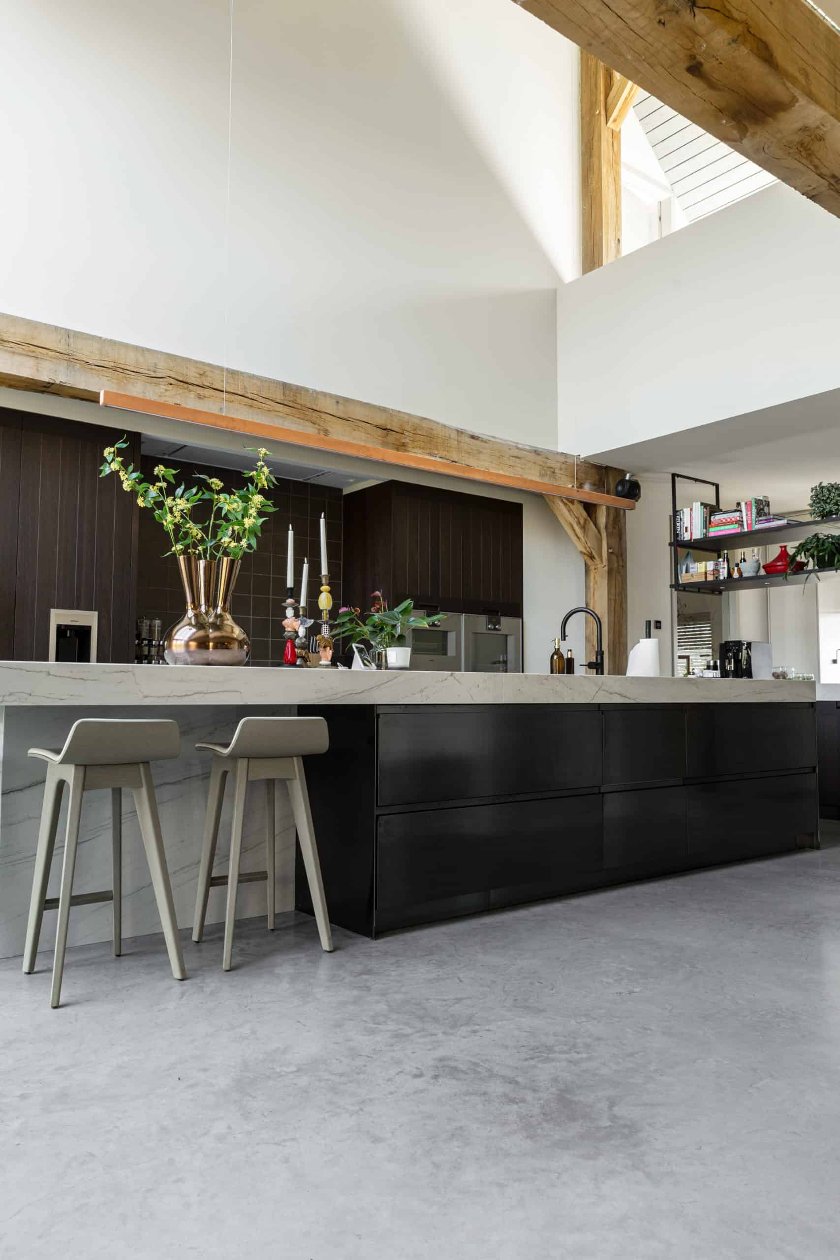 Woning in Oss met een keukeneiland met een marmeren blad en een donkere onderkant gecombineerd met een gevlinderde betonvloer