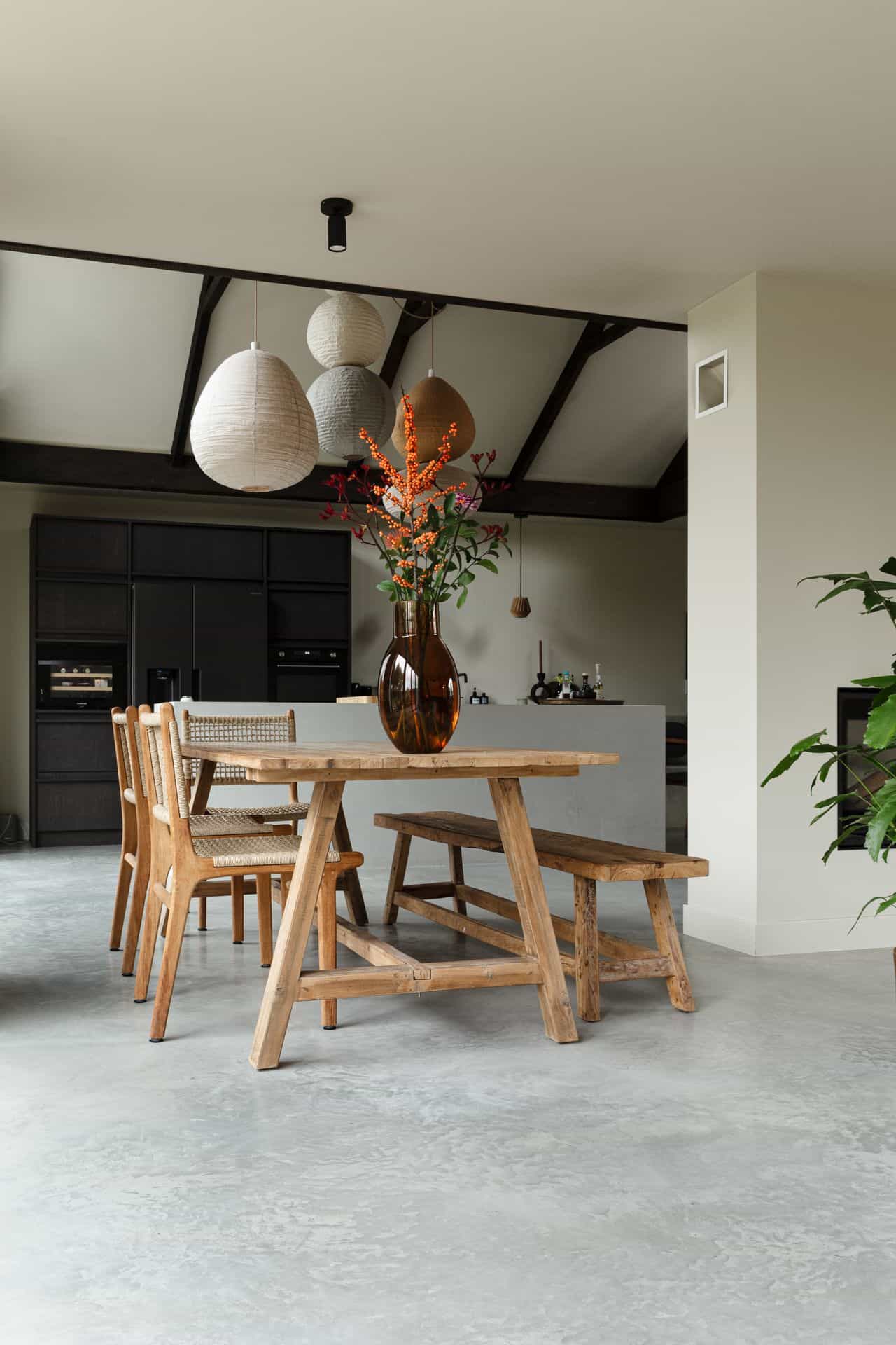 Eetkamer met een gevlinderde betonvloer in Rijnsburg. Hierop staat een houten tafel met houten stoelen en een bankje.