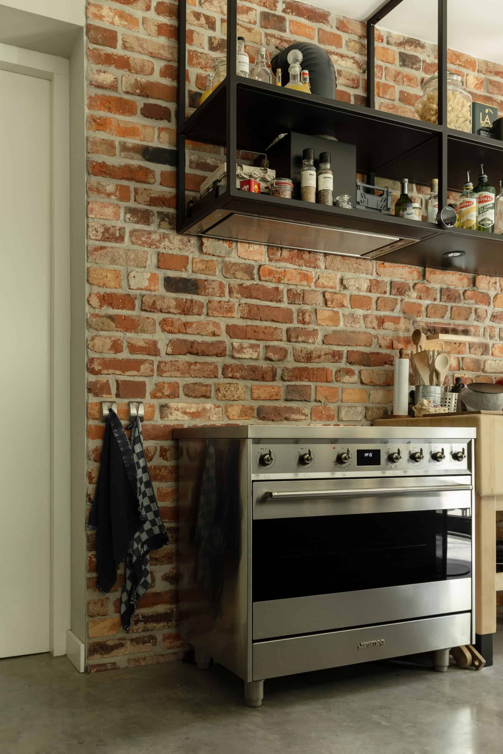 Bakstenen muur in de keuken in Hilvarenbeek met hiervoor een oven. Deze staat op een gevlinderde betonvloer.