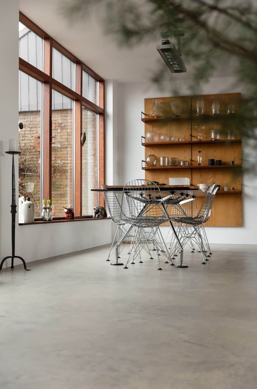 Eetkamer met een houten tafel en ijzeren stoelen op een Italiaanse betonlook vloer in Oostzaan