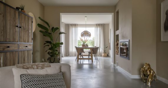 Gevlinderde betonvloer in een vrijstaande woning in Brunssum. Hierop staat een beige stoel, houten tafel met daaraan beige stoelen en een gouden aap.