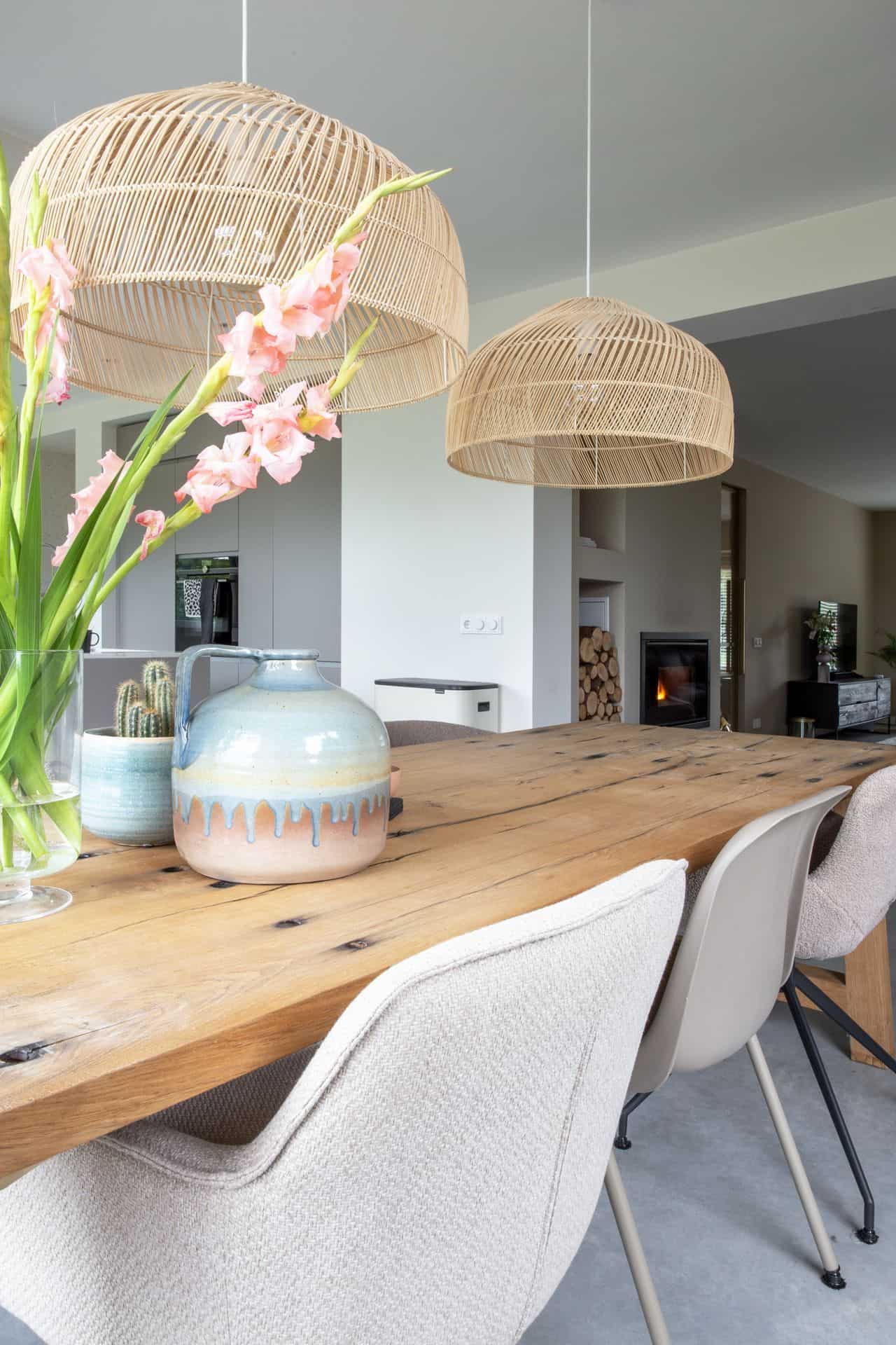 Eetkamer in Brunssum met een houten tafel en beige stoelen. Dit staat op een gevlinderde betonvloer. Aan het plafond hangen rieten lampen.