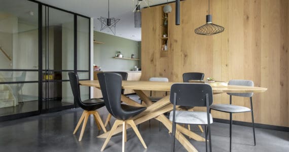 Gevlinderde betonvloer in de eetkamer in Brielle, gecombineerd met een houten tafel, zwarte stoelen en houten kastenwanden