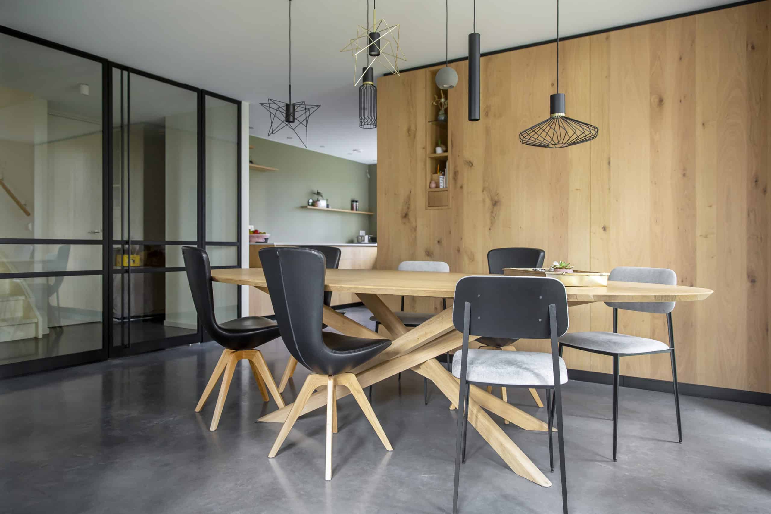 Gevlinderde betonvloer in de eetkamer in Brielle, gecombineerd met een houten tafel, zwarte stoelen en houten kastenwanden