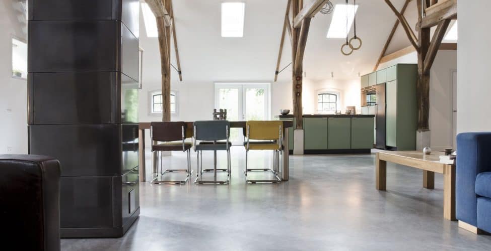 Woon boerderij in Rijswijk met een gevlinderde betonvloer van Willem Designvloeren. Hierop staat een groene keuken en een houten tafel met daaraan verschillende kleuren stoelen.