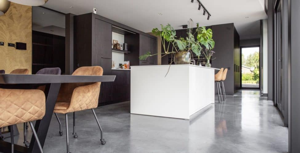 Zwarte keuken met een wit kookeiland in Nuenen, gecombineerd met een gevlinderde betonvloer.
