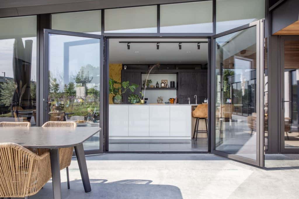 Gevlinderd betonnen terras in Nuenen, gecombineerd met een zwarte tafel. Binnen ligt een gevlinderde betonvloer in de keuken. Hierop staat een wit kookeiland en een zwarte keuken