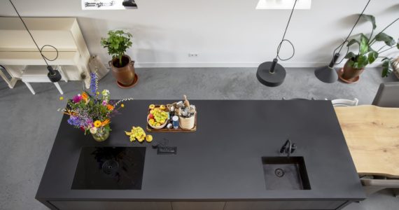 Zwart kookeiland met daaronder een gevlinderde betonvloer van Willem Designvloeren