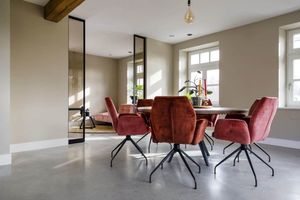 Gevlinderde woon betonvloer in deze eetkamer in Horst. Gecombineerd met een houten eettafel en daaromheen roze stoelen