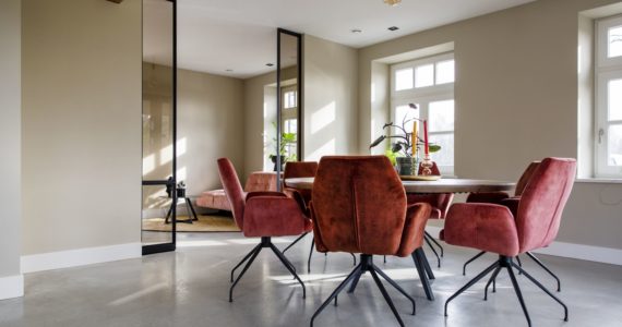 Gevlinderde woon betonvloer in deze eetkamer in Horst. Gecombineerd met een houten eettafel en daaromheen roze stoelen