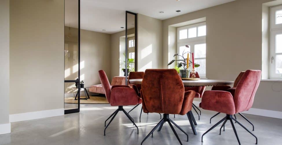 Gevlinderde woon betonvloer in deze eetkamer in Horst. Gecombineerd met een houten eettafel en daaromheen roze stoelen