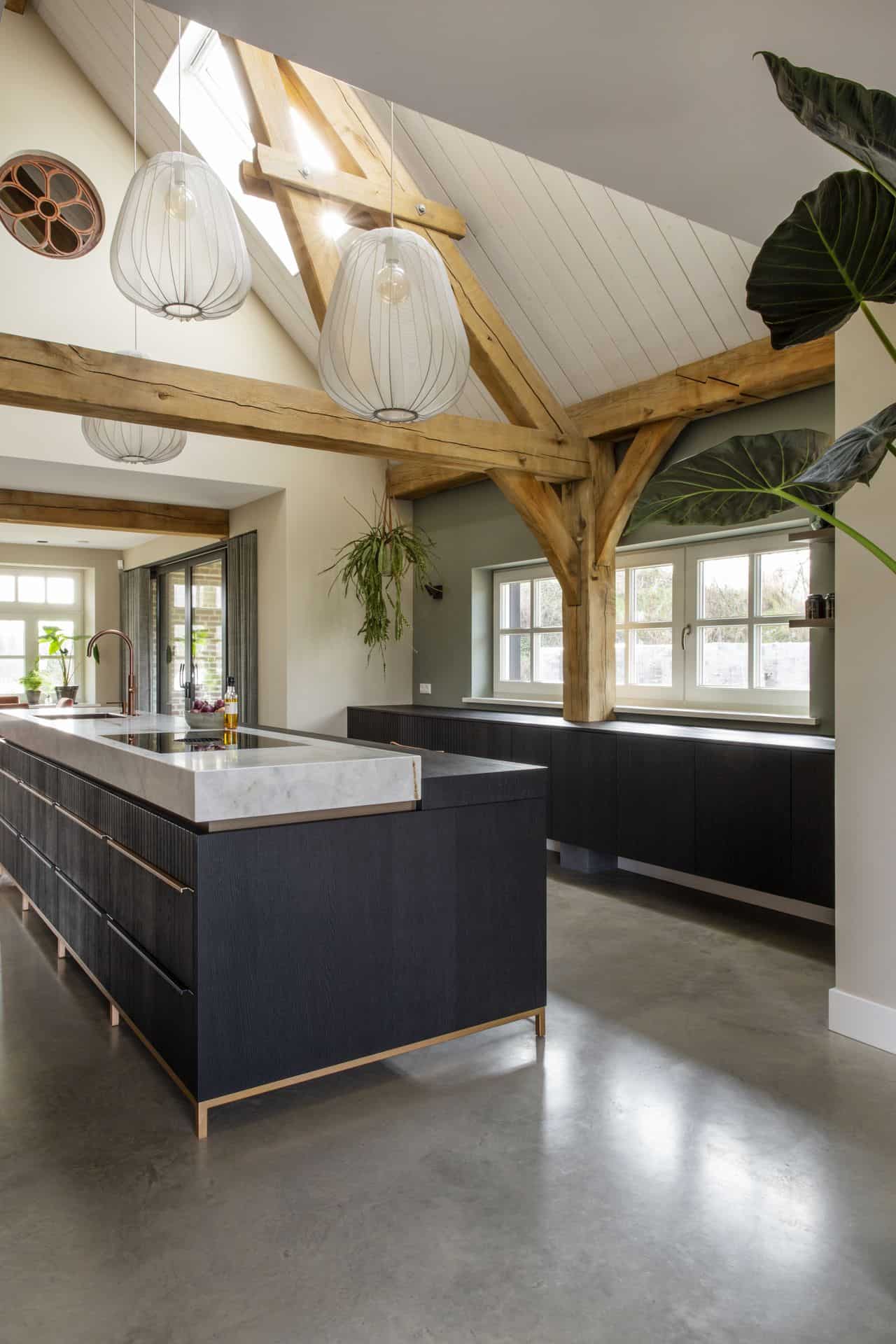 Zwart, marmeren met gouden keuken in Horst. Gecombineerd met een gevlinderde betonvloer, houten balken en groene en witte wanden